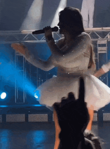 a woman in a white dress singing into a microphone on a stage
