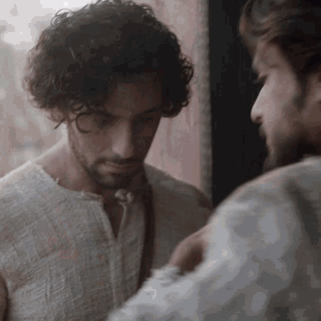 a man with curly hair and a beard looks down at something