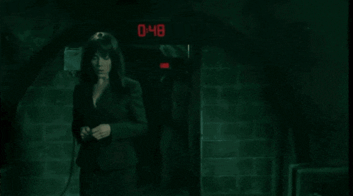a woman in a suit stands in front of a clock that says 0:44