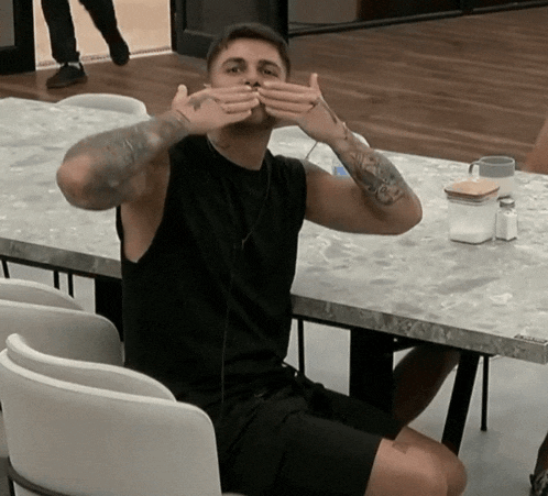 a man with a tattoo on his arm covering his mouth with his hands