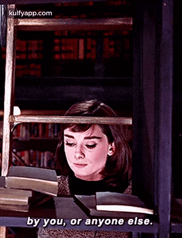 a woman is reading a book in a library and saying by you , or anyone else .
