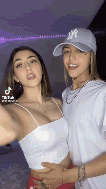 two women are posing for a picture together and one of them is wearing a hat with the letter ny on it .