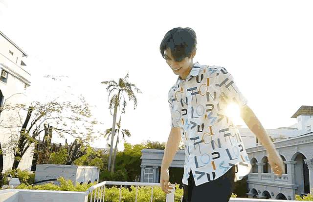 a man wearing a shirt with letters on it is standing in front of palm trees