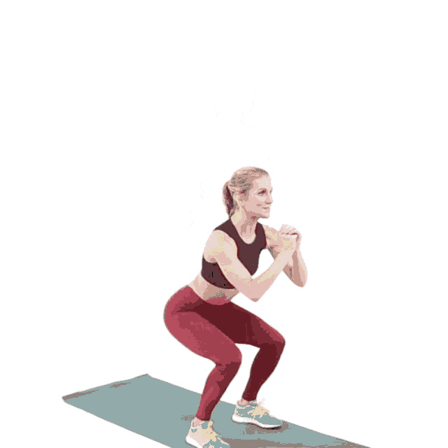 a woman in a black top and red pants is jumping on a mat