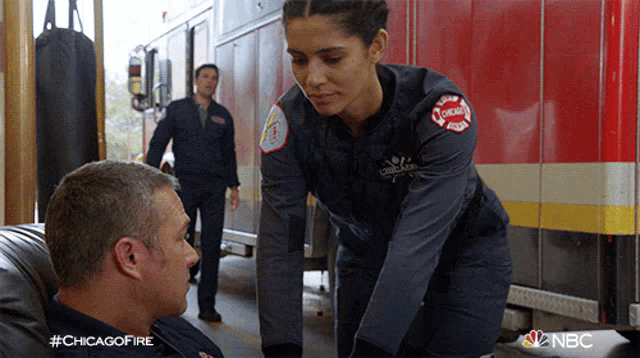 a woman in a chicago fire uniform talks to a man in front of a fire truck