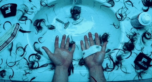 a person 's hands are laying on a sink covered in hair and shaving supplies