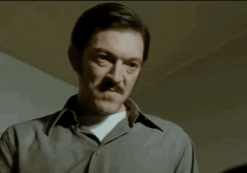 a man with a mustache is pointing at the camera
