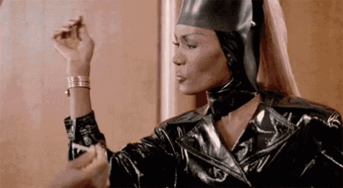 a woman wearing a black leather jacket and a rubber hat is applying lipstick to her wrist .