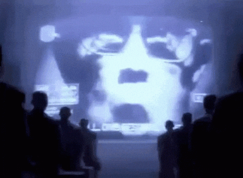 a group of people are standing in front of a screen with a picture of a man 's face on it .