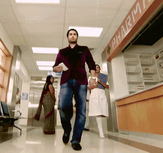 a man walks down a hallway in front of a pharmacy sign