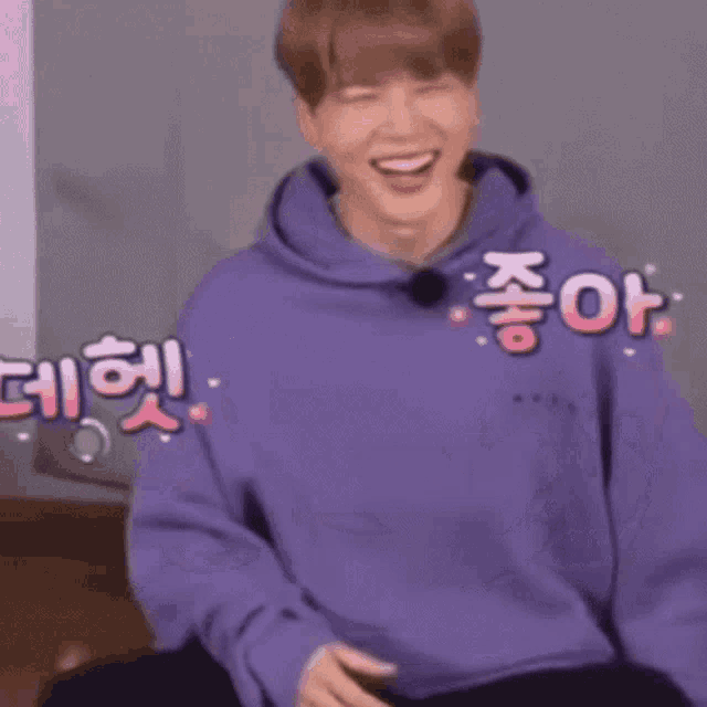 a man in a purple hoodie is sitting on a chair and making a funny face .