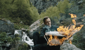 a man is sitting on a rock holding a piece of paper that is burning