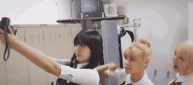 three girls are taking a selfie in a locker room with a camera