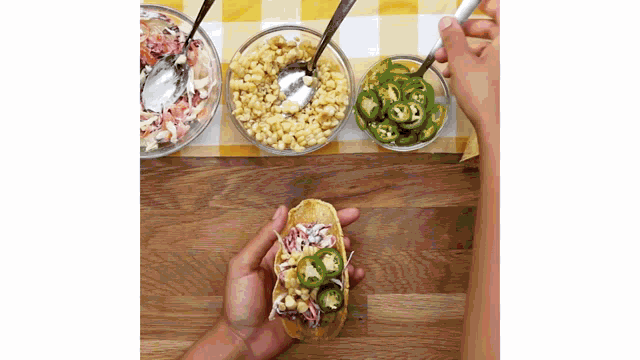 a person is making a taco with corn jalapenos and coleslaw on a wooden table .