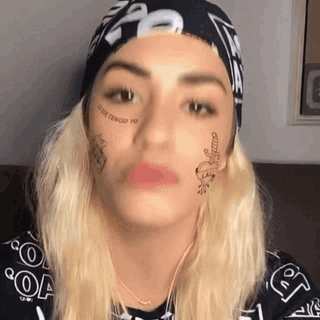 a woman with tattoos on her face is wearing a bandana and a hat .