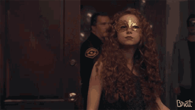 a woman with red hair is wearing a mask and the word brat is on the bottom right