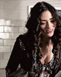 a woman with curly hair wearing a black jacket and a plunging neckline