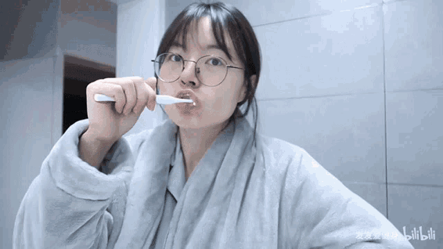 a girl with glasses is brushing her teeth in front of a wall that says bilibili