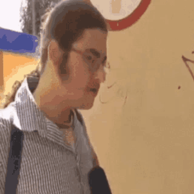 a man wearing glasses and a ponytail stands in front of a wall that has the word joy written on it
