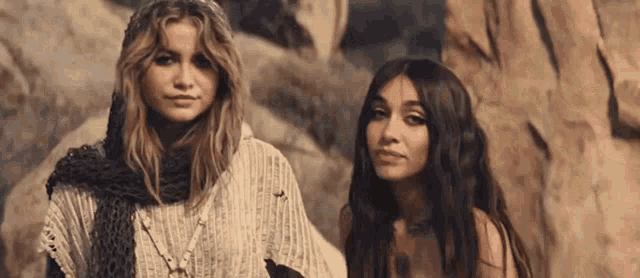 two women are standing next to each other in front of a rock formation