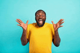 a man in a yellow t-shirt is laughing with his mouth open and his hands in the air .