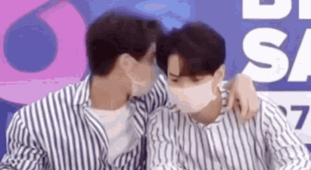 two men wearing masks are hugging each other in front of a sign .
