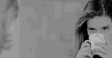a black and white photo of a woman drinking from a white cup .