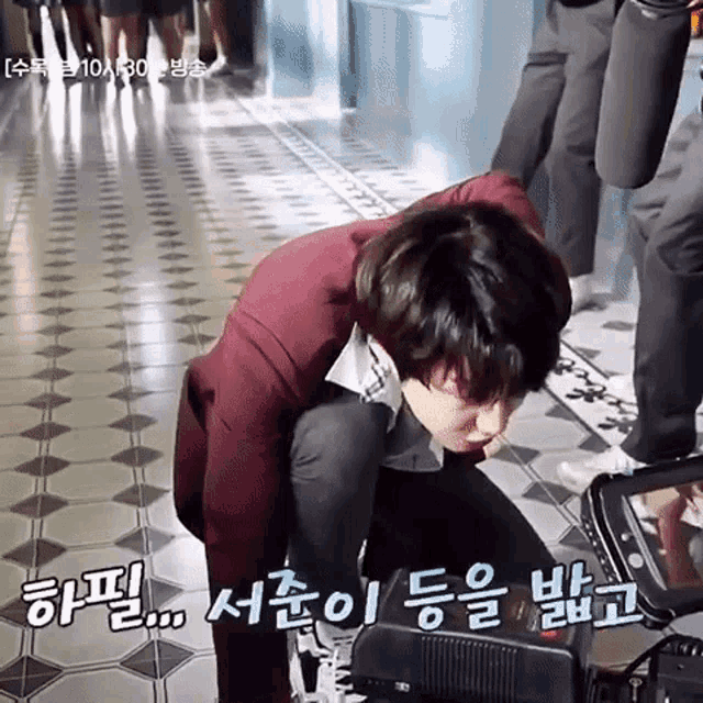 a man in a suit is kneeling down next to a camera with korean writing on the floor