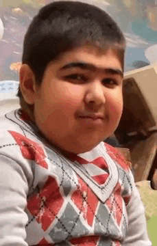 a young boy is making a funny face while wearing a sweater and looking at the camera .