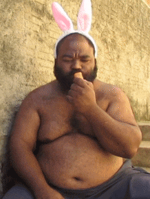 a shirtless man wearing bunny ears is eating an ice cream