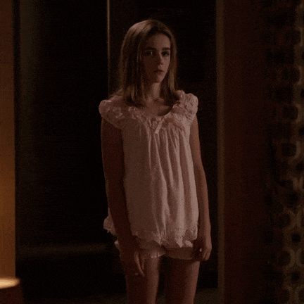 a young girl in a pink dress and shorts is standing in a dark room