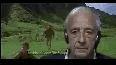an older man wearing headphones is standing in a field with a man running in the background .
