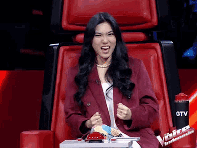 a woman in a red jacket is sitting in a red chair on a television show .
