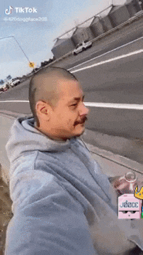a man with a shaved head and a mustache is sitting on the side of the road .