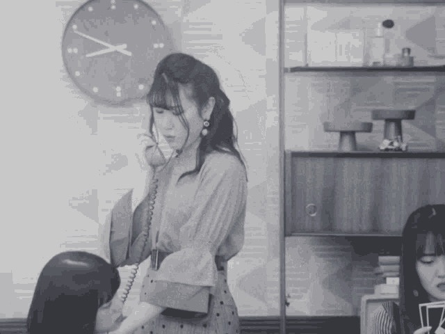 a black and white photo of a woman talking on a phone with a clock in the background