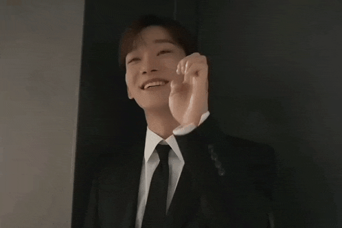 a man in a suit and tie is smiling and holding his hand up
