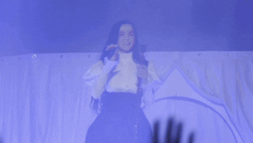 a woman singing into a microphone with a crowd behind her