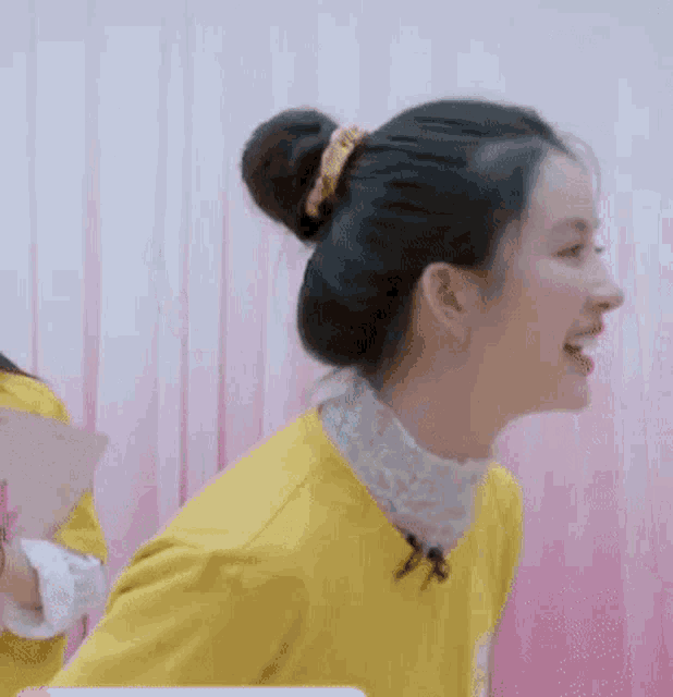 a woman in a yellow shirt with a bun on her head is smiling .