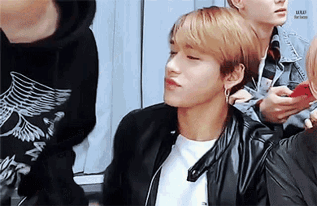 a young man wearing a black leather jacket is sitting in a room with other people .