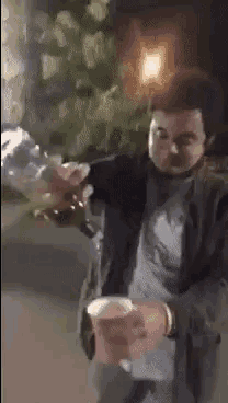 a man is holding a cup of coffee and a bottle of beer in his hand .