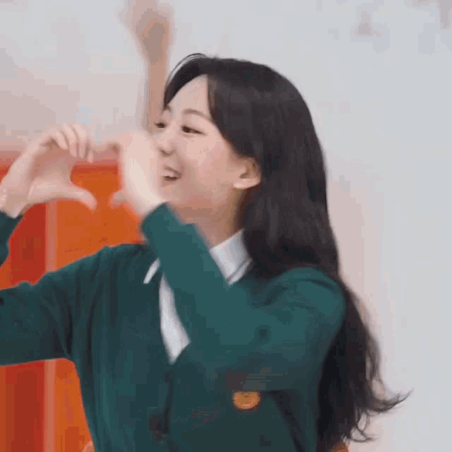 a young woman in a green sweater is making a heart shape with her hands .