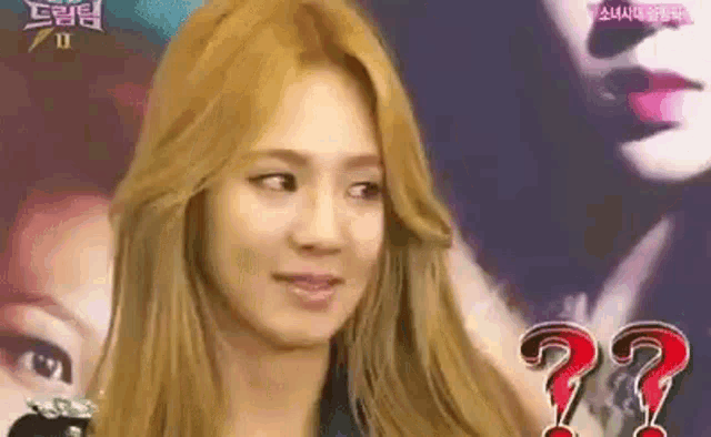 a woman with blonde hair is making a funny face in front of a picture of a woman with a question mark on her face .