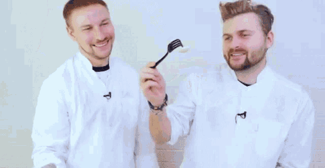 two men in white coats are holding a fork with a spoon in it .