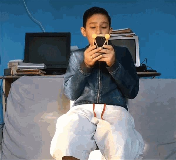 a young boy is sitting in front of a computer and holding a cell phone in his hand