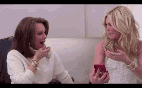 two women are sitting next to each other looking at their phones .