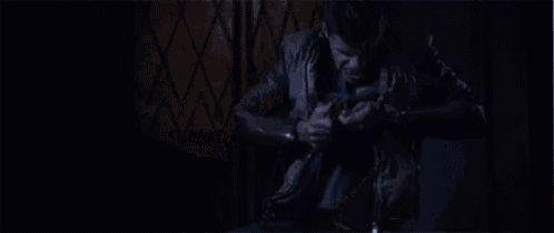 a shirtless vampire is standing in a dark room with his mouth open .