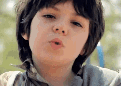 a close up of a young boy blowing a kiss