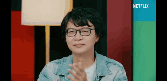 a man wearing glasses is applauding in front of a netflix sign .
