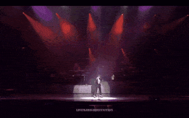 a man is dancing on a stage in front of a microphone while wearing a white hat .