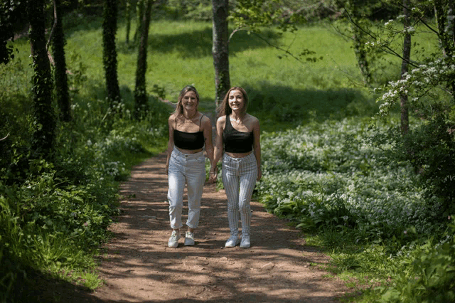 two women are walking down a path in the woods holding hands
